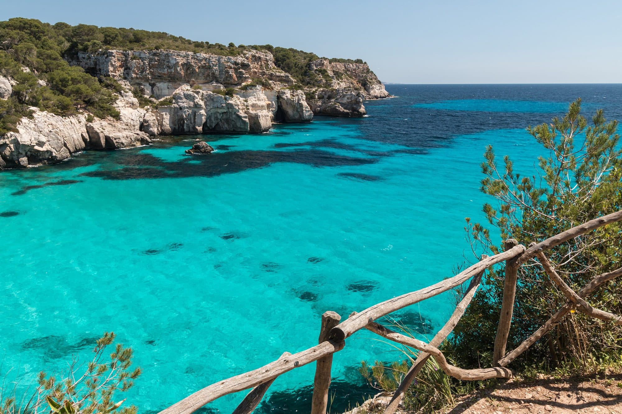 Cala Macarella desde el acantilado: agua turquesa entre pinos y rocas blancas